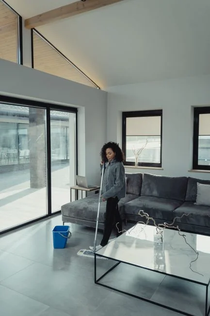 A professional cleaner in red coveralls vacuuming a modern living room with a yellow vacuum cleaner.