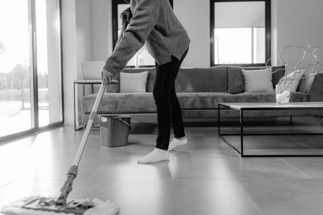 A grayscale photo showing a person mopping the floor in a modern living room.
